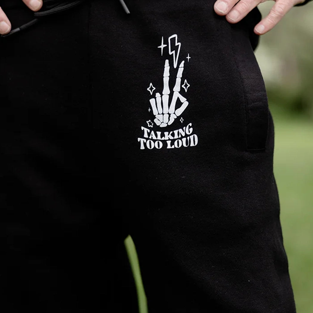 model wearing a black sweat pants that has Skelton fingers with lighting bulb that says Talking Too Loud.
