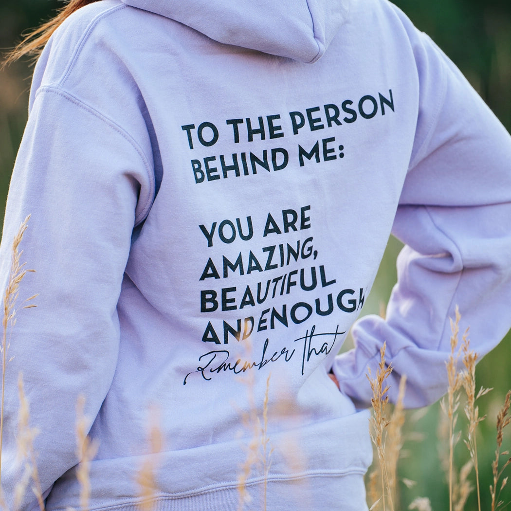 Model wearing a lavender graphic apparel hoodie that says To the person behind me: you are amazing, beautiful and enough. Remember that. The design is text only in black.