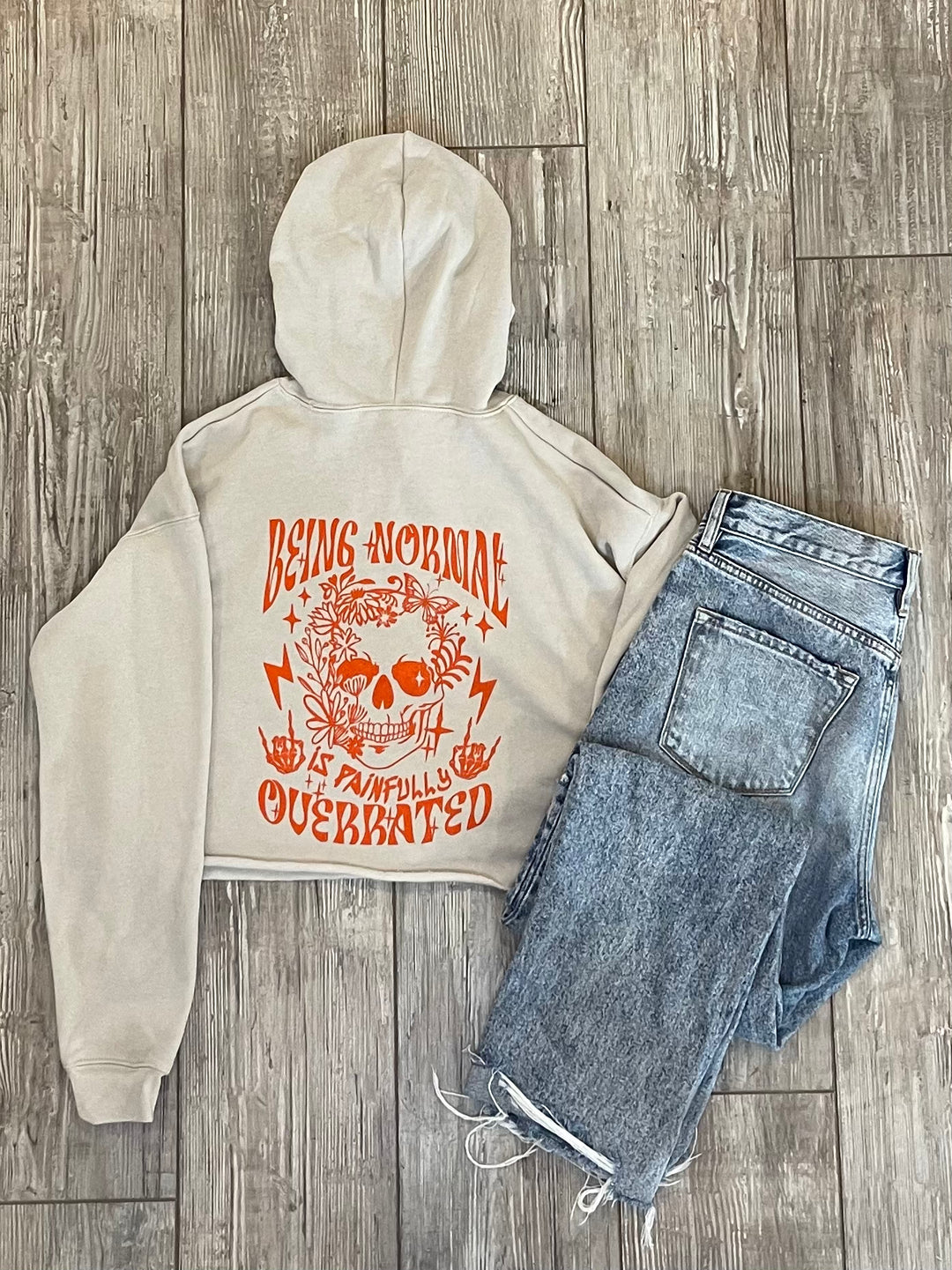 Being normal is painfully overrated Skelton with rock fingers, lighting stripes, flowers and butterflies, tan crop top hoodie with jeans 