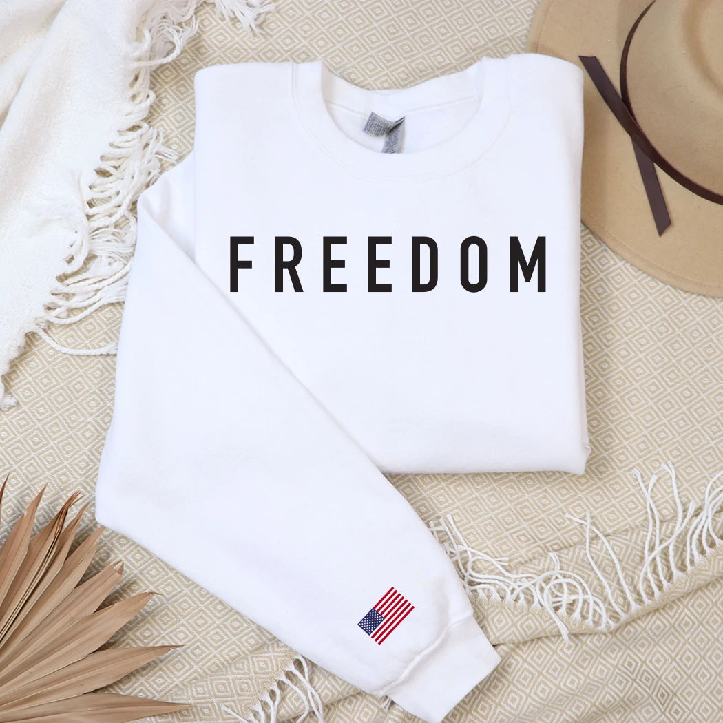 White crewneck sweatshirt with "FREEDOM" text and an American flag on the sleeve.