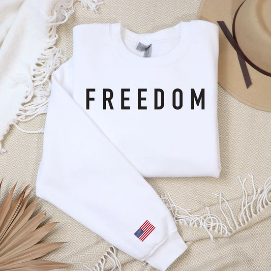 White crewneck sweatshirt with "FREEDOM" text and an American flag on the sleeve.