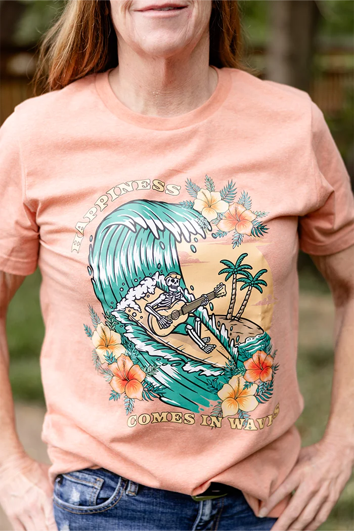 Happiness comes in waves design on a heather sunset t-shirt. Skeleton on surfboard playing guitar on wave with flowers and sunset. Yellow, orange and teal design. 