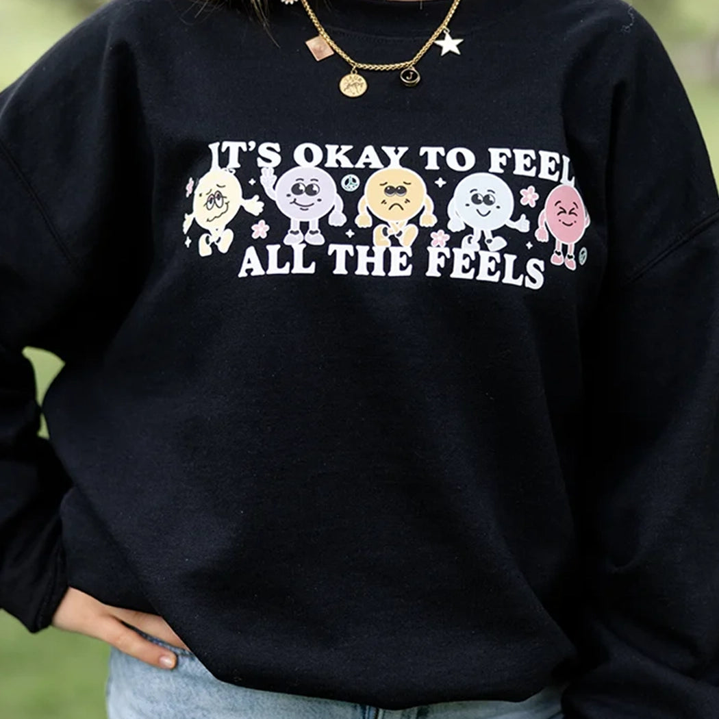 It’s okay to feel all the feels positive message shirt with smiley face characters. Black crewneck with colorful design. 