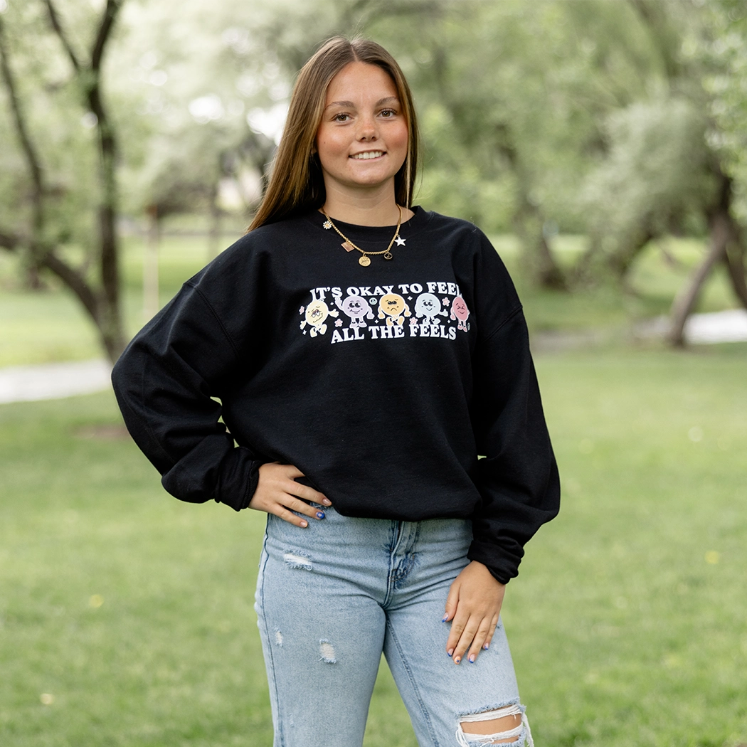 It’s okay to feel all the feels positive message shirt with smiley face characters. Black crewneck with colorful design. 