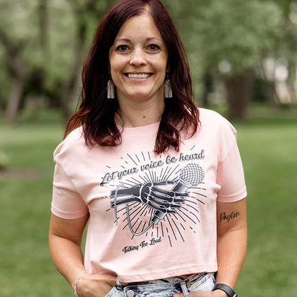 Pink crop top shirt with positive message that says Let Your Voice Be Heard. The design has a Skelton hand with a microphone.  