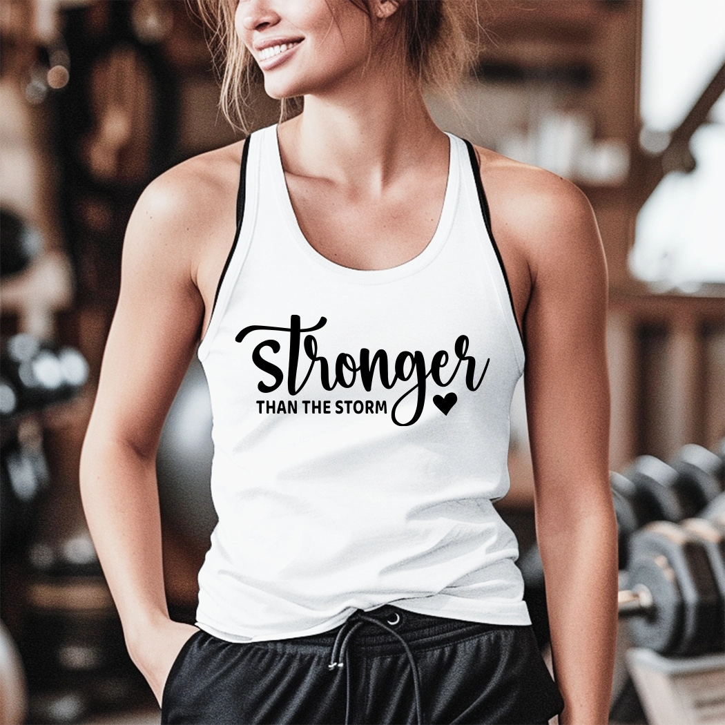 The workout tank has the text "Stronger Than The Storm" printed on it. The text is in a large, bold font and is centered on the tank. The tank is a light gray color and appears to be made of a soft, breathable fabric. It has a racerback style, which is designed to provide a full range of motion for the wearer. The tank is also moisture-wicking, which helps to keep the wearer cool and dry during exercise.