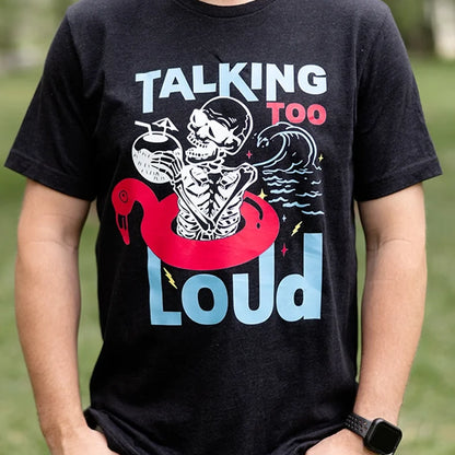 Black Talking Too Loud shirt with wave, skeleton in a pink flamingo floaty with a coconut drink. Design is blue, pink and white. 