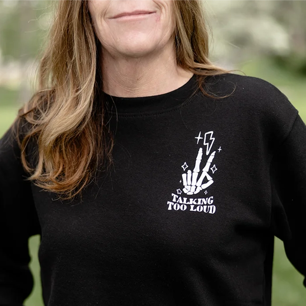 model wearing a black crewneck that has Skelton fingers with lighting bulb that says Talking Too Loud. 