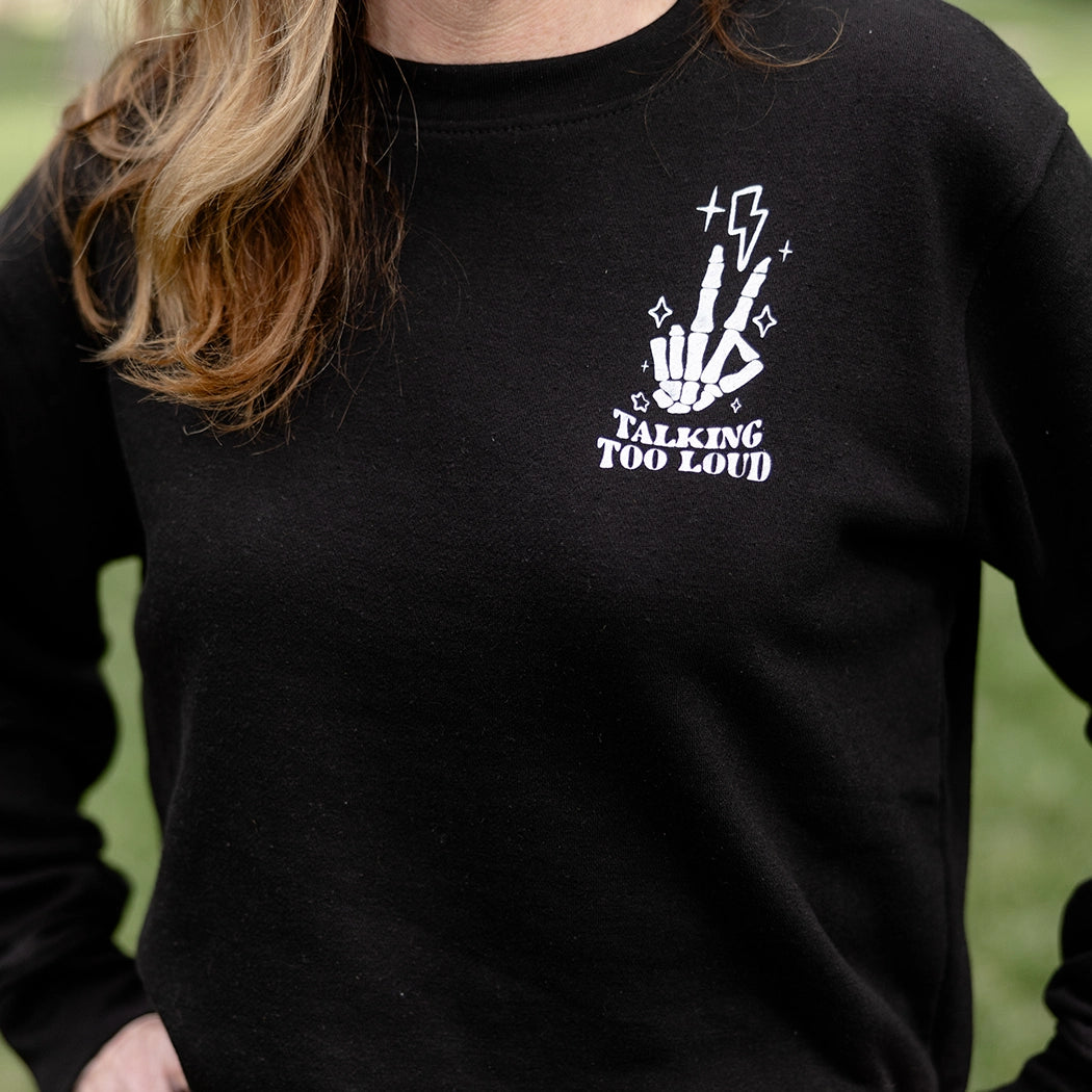 model wearing a black crewneck that has Skelton fingers with lighting bulb that says Talking Too Loud. 