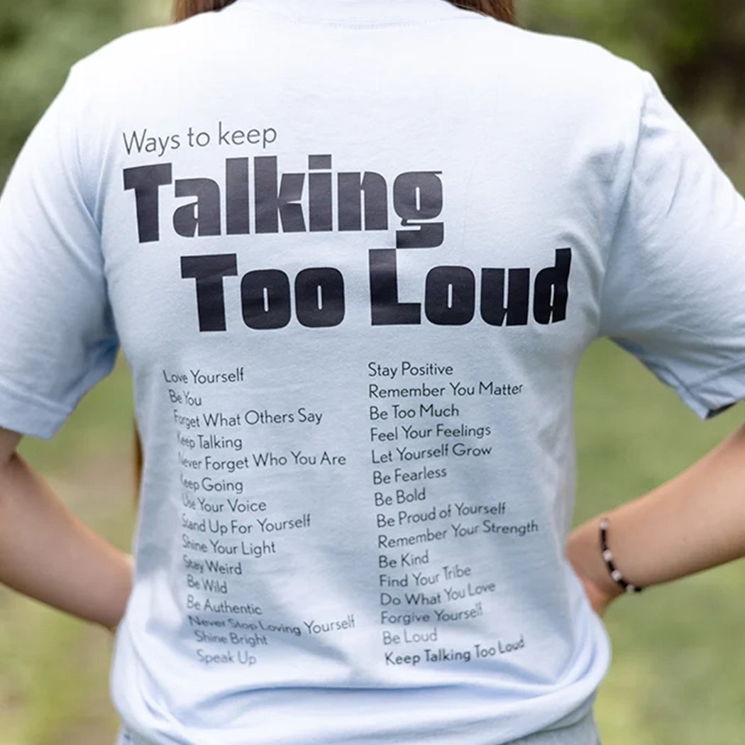 Woman wearing  blue graphic tee with saying "Ways to keep Talking Too Loud"