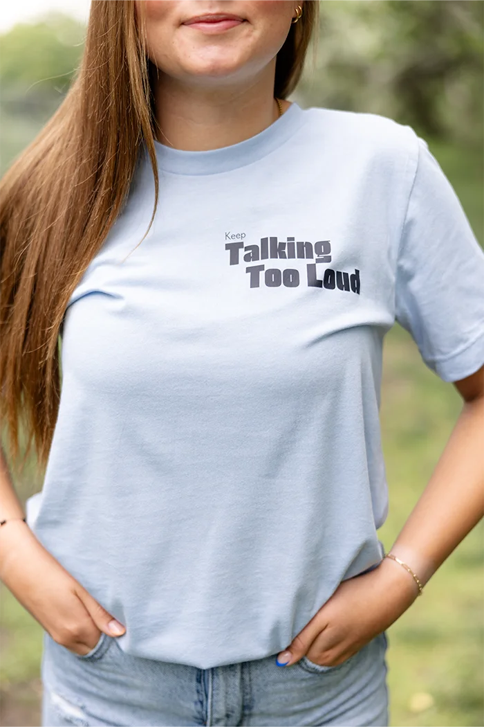 Woman wearing  blue graphic tee with saying "Ways to keep Talking Too Loud"