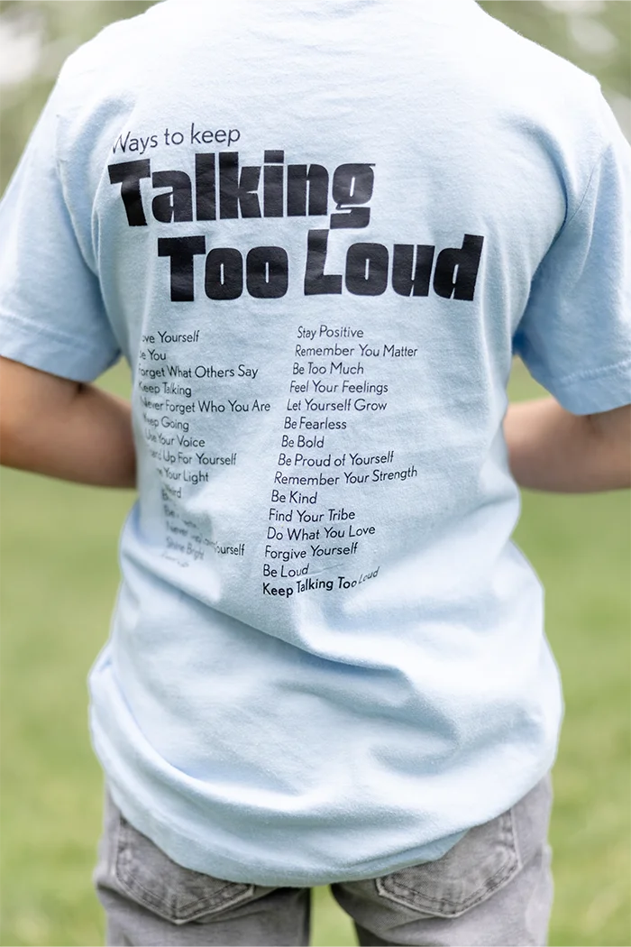 Kid wearing  blue graphic tee with saying "Ways to keep Talking Too Loud"