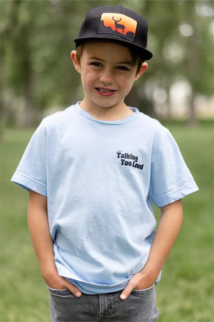 Kid wearing  blue graphic tee with saying "Ways to keep Talking Too Loud"