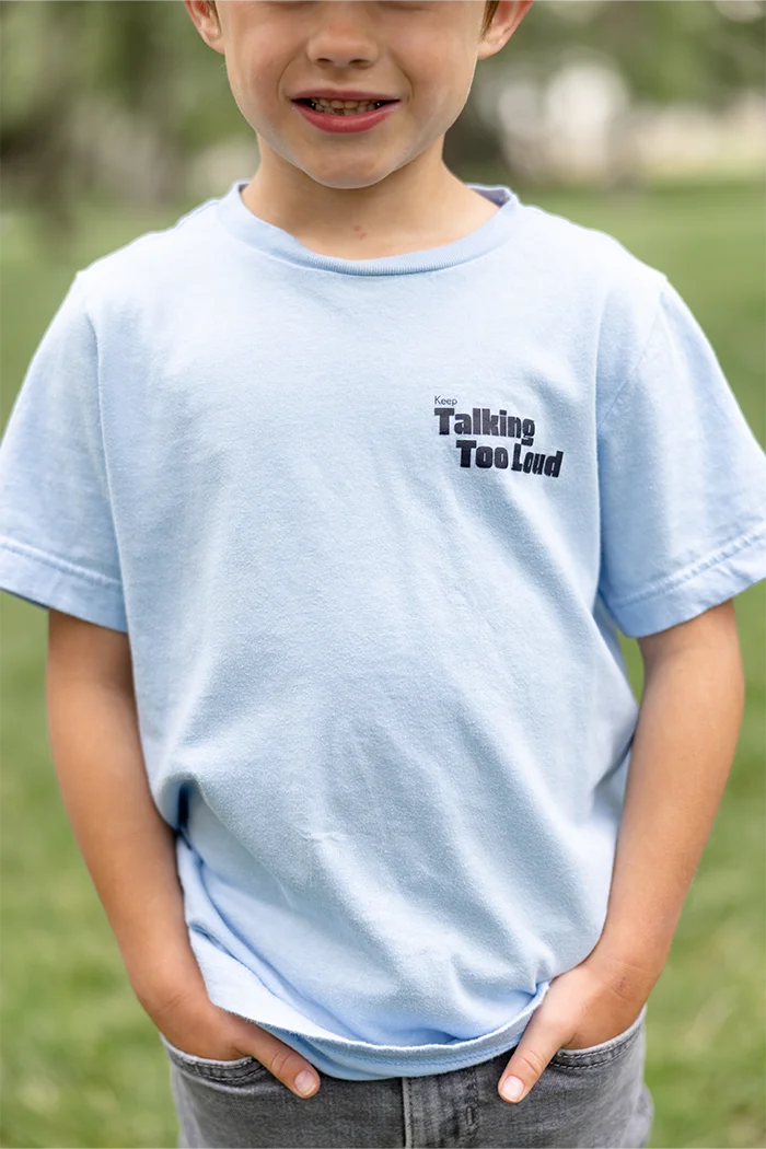 Kid wearing  blue graphic tee with saying "Ways to keep Talking Too Loud"