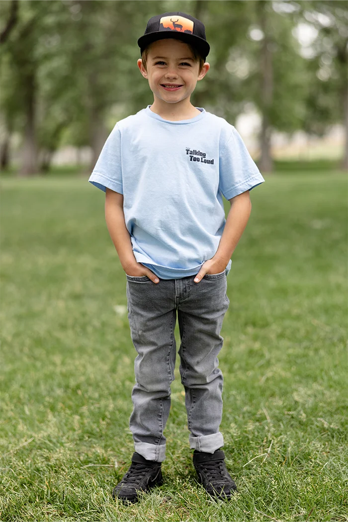 Kid wearing  blue graphic tee with saying "Ways to keep Talking Too Loud"