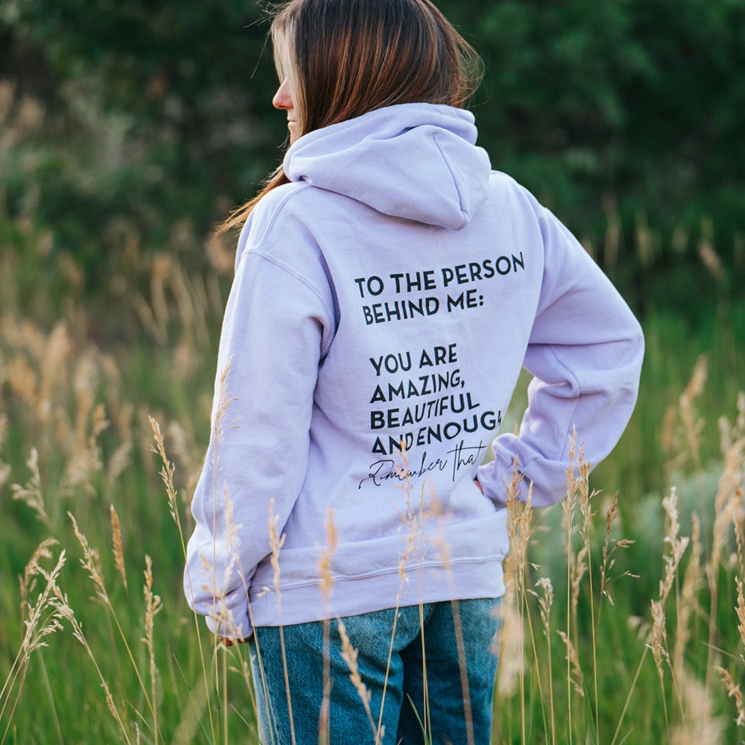 Model wearing lavender shirt that says To the person behind me: you are amazing, beautiful and enough. Remember that. The design is text only in black.