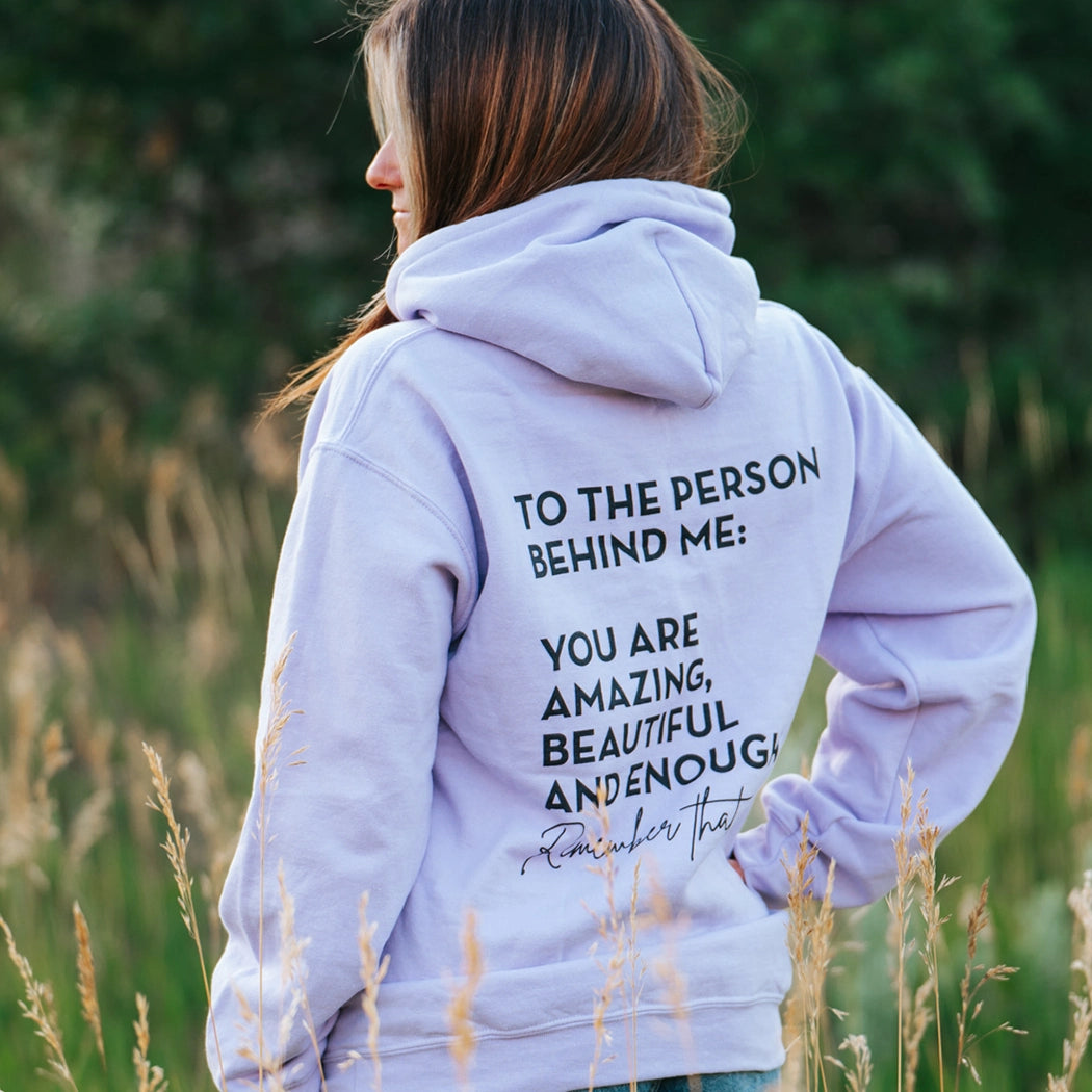 Model wearing lavender shirt that says To the person behind me: you are amazing, beautiful and enough. Remember that. The design is text only in black.