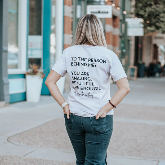 Model wearing lavender shirt that says To the person behind me: you are amazing, beautiful and enough. Remember that. The design is text only in black.