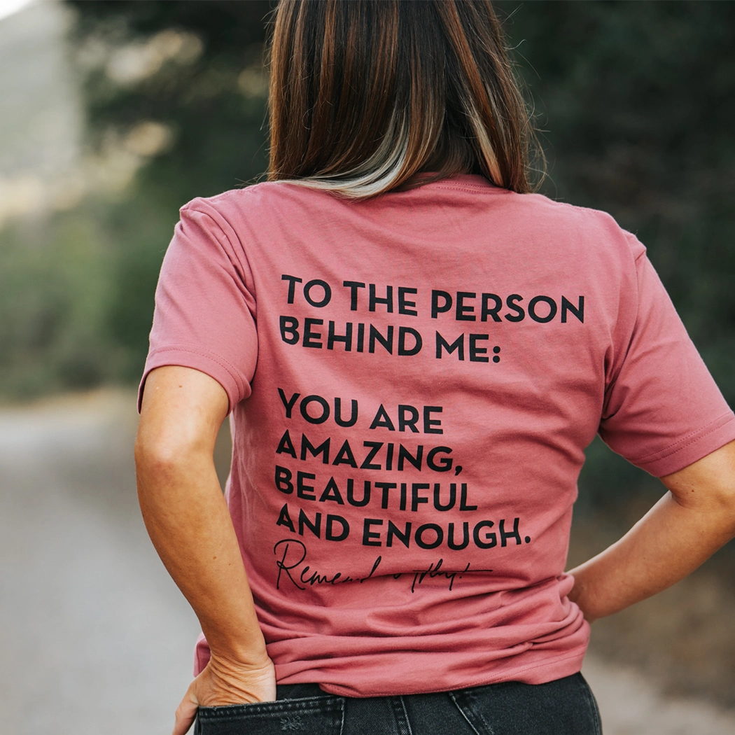 Model wearing mauve shirt that says To the person behind me: you are amazing, beautiful and enough. Remember that. The design is text only in black.